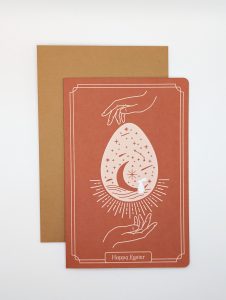Artistic Easter greeting card featuring hands encircling a star-filled egg with an envelope behind it